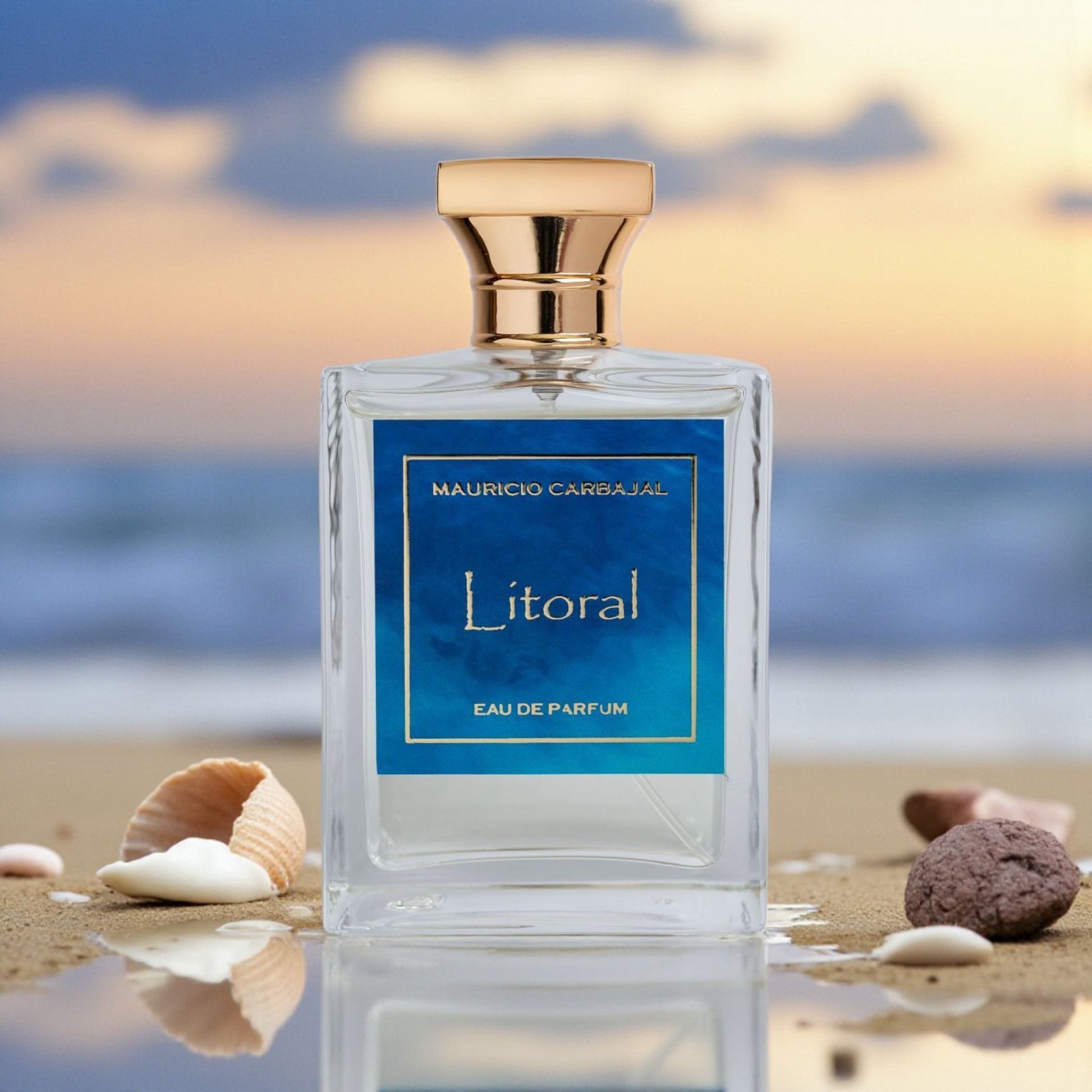 frasco del perfume Litoral de Mauricio Carbajal en la orilla con arena y conchitas marinas en el fondo el atardecer